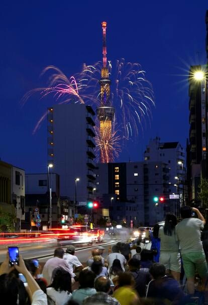 東京スカイツリーの上空に開く花火と、道路沿いで見上げる人々